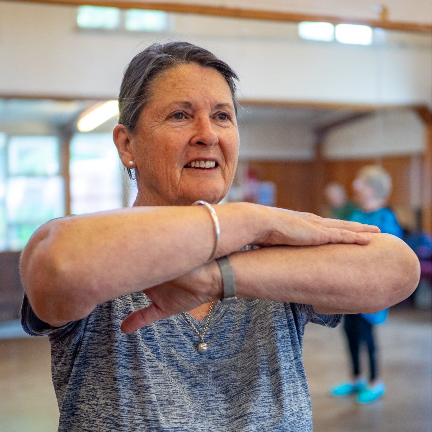 A pakeha woman in a grey Tshirt holds her arms up folded in front of her